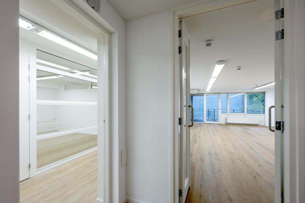 Doorkijk vanuit een gang naar twee moderne, lichte kantoorruimtes aan de Prins Hendrikkade met houten vloer en grote ramen.